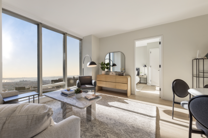 living room with sofa, white walls, & large windows looking out on NYC view